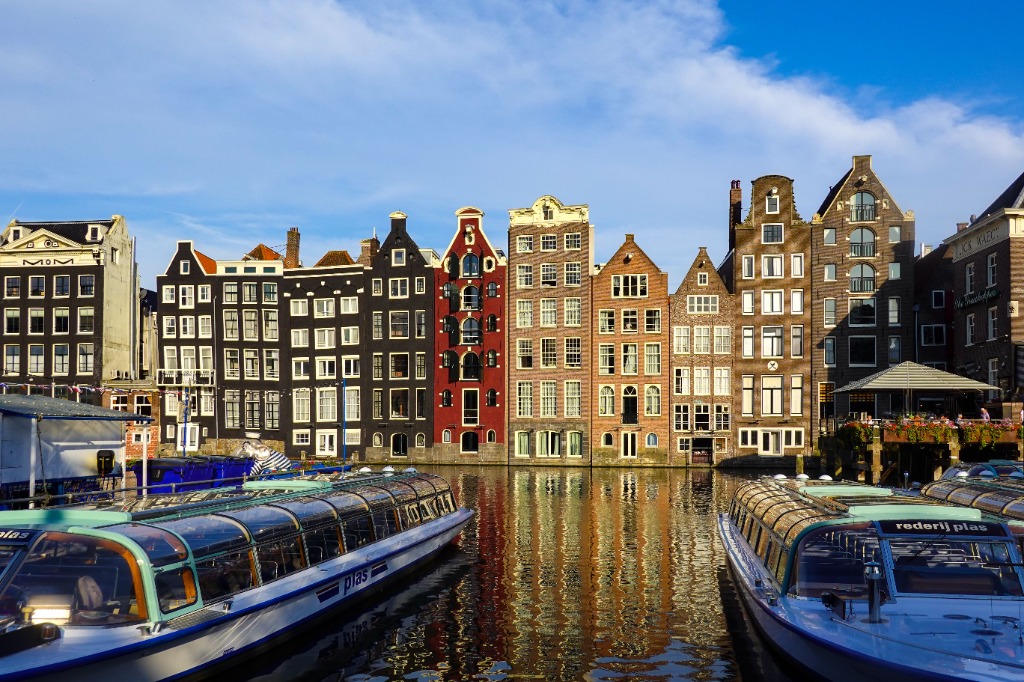 Colorful dancing canal houses of Amsterdam reflected in the water with canal tour boats in the foreground
