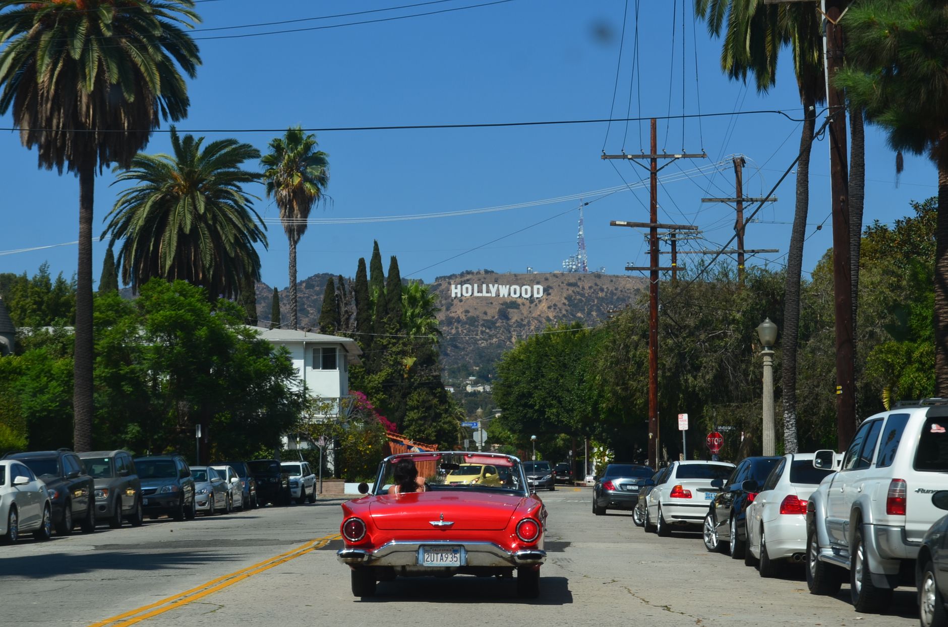 Red convertible heading toward the Hollywood Sign under bright California sun.